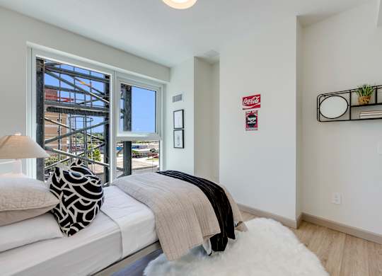 A bedroom with a bed, a lamp, and a window overlooking a construction site.