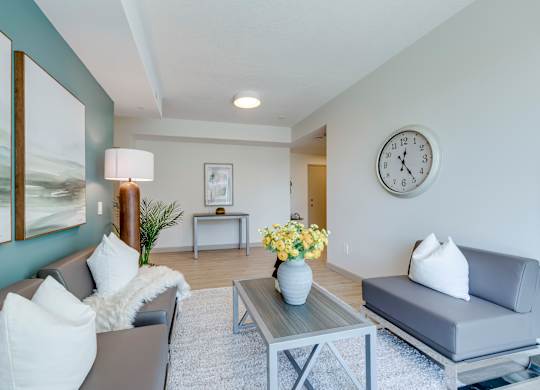 A living room with a grey couch, a coffee table, and a clock on the wall.