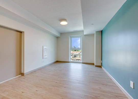 A room with a wooden floor and a window overlooking a balcony.