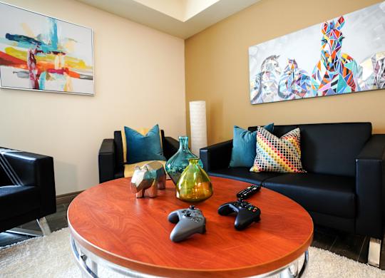 A living room with a black couch, a wooden table, and two gaming controllers on the table.
