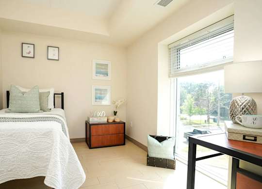 A bedroom with a bed, nightstand, and a table with a lamp.
