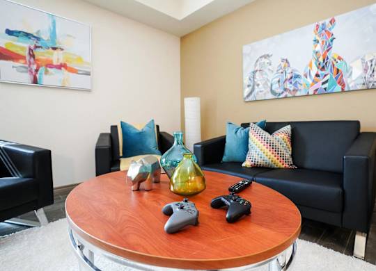 A living room with a black couch, a wooden table, and two Xbox controllers on it.
