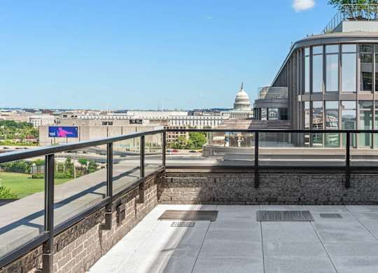 A penthouse balcony with a view of the U.S. Capitol and a building with a glass facade.