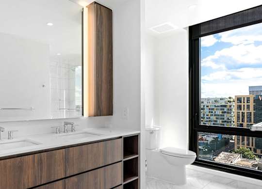 A modern penthouse bathroom with a large mirror and wooden cabinets.