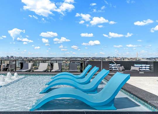 A pool with blue chairs and a cityscape in the background.