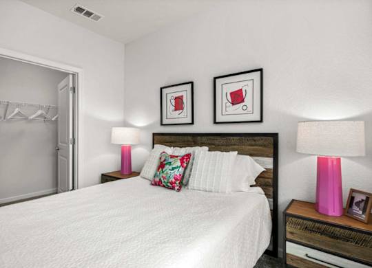 A bedroom with a large bed, two pink lamps, and two framed pictures on the wall.