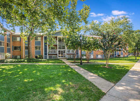 A sunny day at a well-kept apartment complex with green grass and trees.