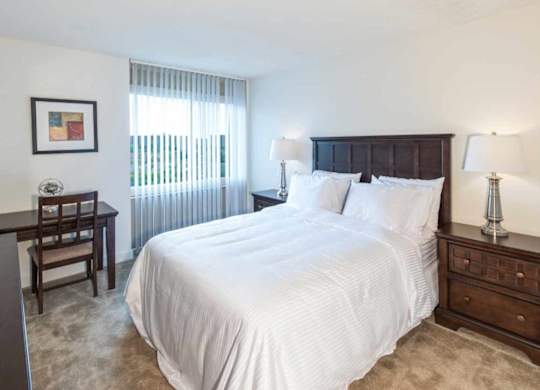 A bedroom with a large bed, a wooden nightstand, and a window with blinds.