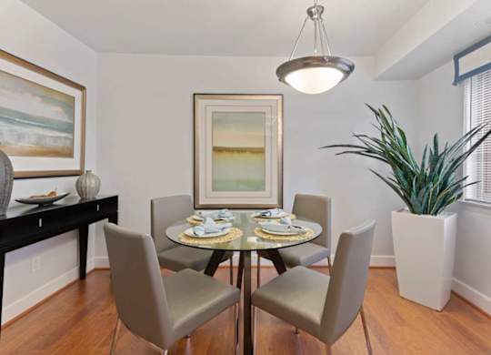 A dining room with a table set for two and a potted plant.