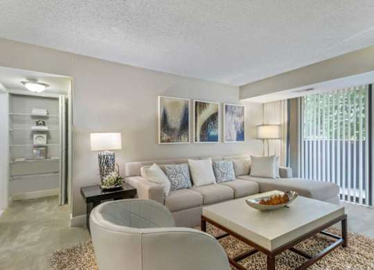 A living room with a white couch, a glass table, and a painting on the wall.