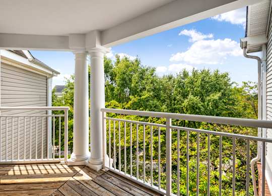 the view from the deck of a home with white columns and a view of trees