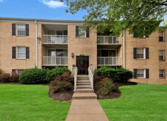 an apartment building with a green lawn and a sidewalk