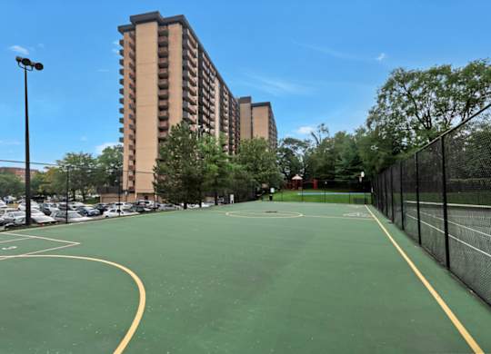 A basketball court is surrounded by a parking lot and apartment buildings.