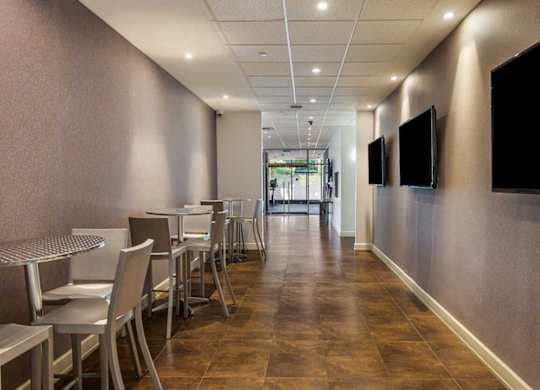 A long hallway with chairs and tables on the left and two TVs on the wall.
