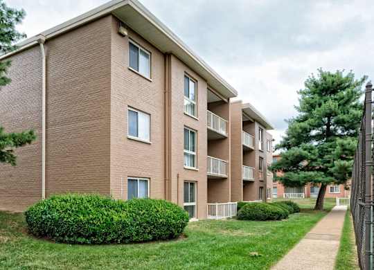 A brown brick apartment building with green bushes in front.