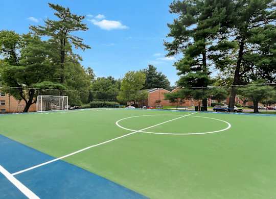 A basketball court with a green and blue surface is surrounded by trees.