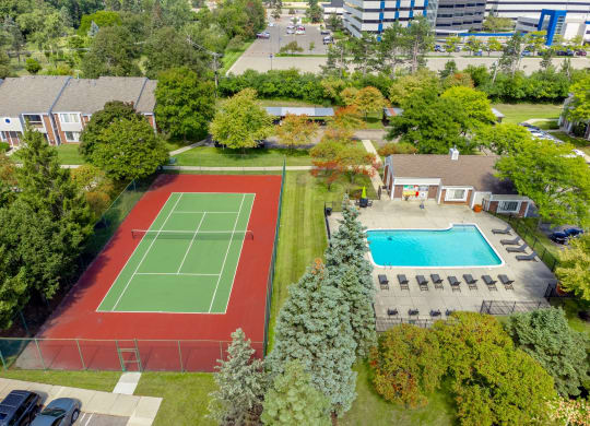 an aerial view of a tennis court and a swimming pool in a backyard with trees
