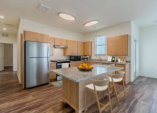 A kitchen with a refrigerator, island, and chairs.
