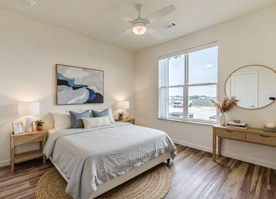 A bedroom with a large bed, a painting on the wall, and a round mirror on the dresser.