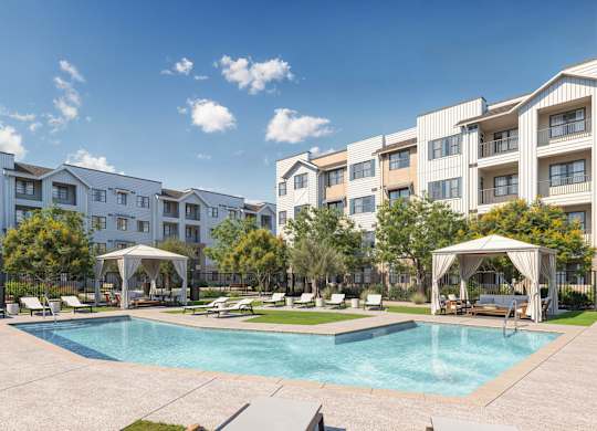 A swimming pool surrounded by lounge chairs and umbrellas in front of apartment buildings at Orchard Springs 55+ Apartment , Surprise, 85374
