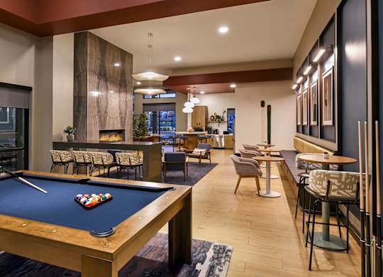 A pool table is in the middle of a room with a bar and chairs.