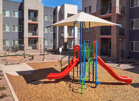 A playground with a red slide and a white umbrella.