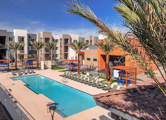 A swimming pool is surrounded by lounge chairs and palm trees.