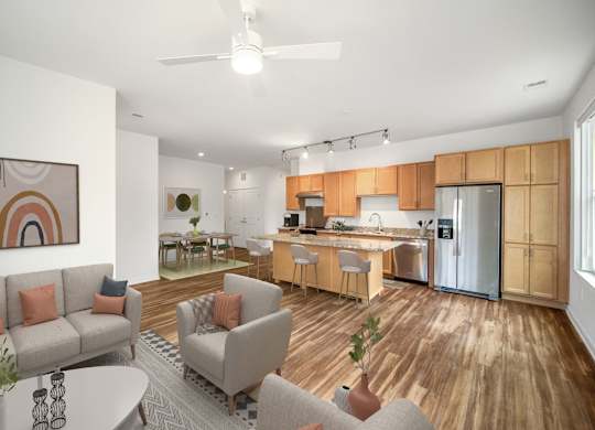 A modern living room with a grey sofa, a grey armchair, a wooden floor, and a kitchen in the background.at Creekridge on the Park, North Carolina, 28212