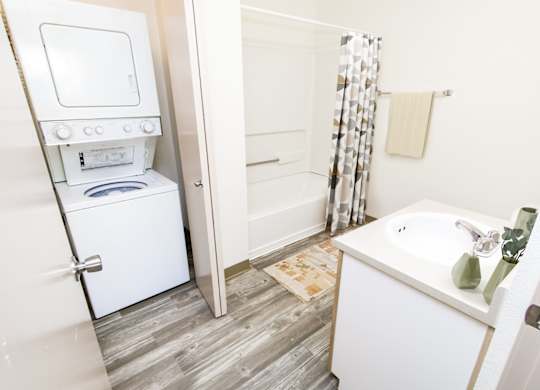 A white washing machine is in a small bathroom with a white sink.
