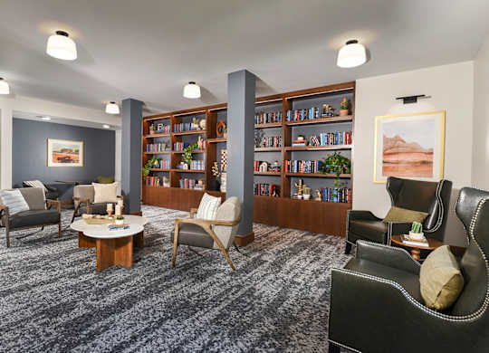 A living room with grey carpet and a bookshelf filled with books.