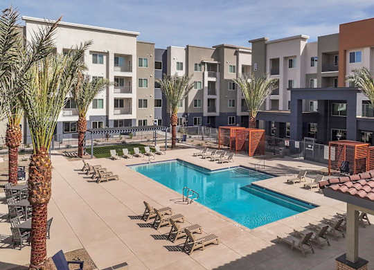 A pool surrounded by palm trees and chairs in front of apartment buildings.