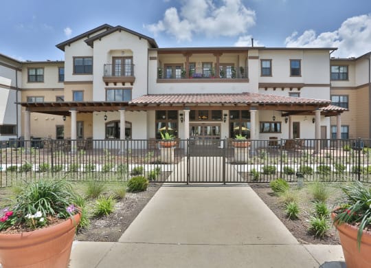 a building with a walkway and a gate in front of it at Cedars of Elk Drive 55+ Apartments, Burleson, 76028