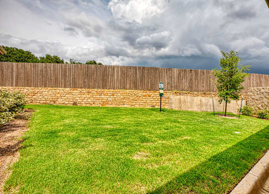 a backyard with a brick wall and a green lawn at Mariposa at South Broadway, Texas, 76058