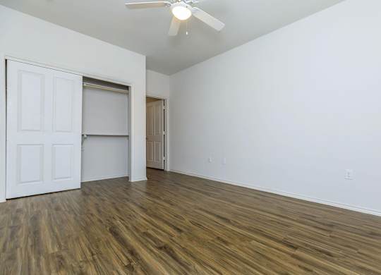 a bedroom with white walls and wood flooring and a closet at Mariposa at Westchester, Grand Prairie, TX