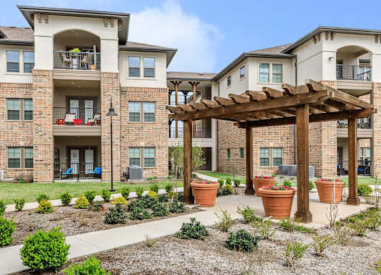 an outdoor area with potted plants in front of an apartment building at Mariposa at Westchester, Grand Prairie, 75052