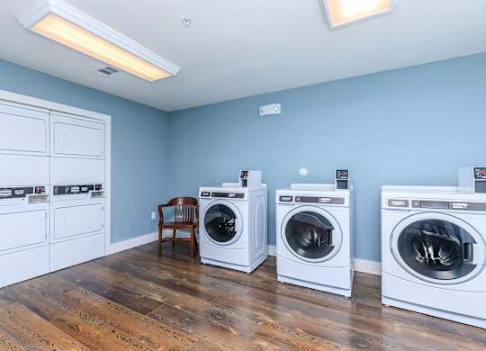 a laundry room with four washing machines and a chair at Mariposa at Westchester, Texas, 75052
