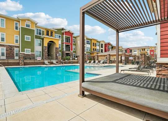 A pool area with a sun lounger and a building in the background.