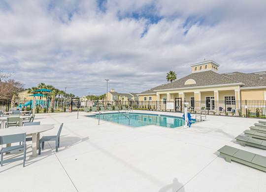 A pool area with sun loungers and a building in the background.