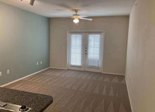 an empty living room with a ceiling fan and a door to a balcony