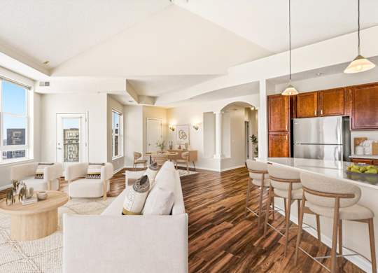 A spacious living room with white furniture and a large window overlooking the city.