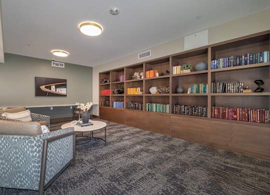 A living room with a grey patterned chair and a coffee table in front of a bookshelf.