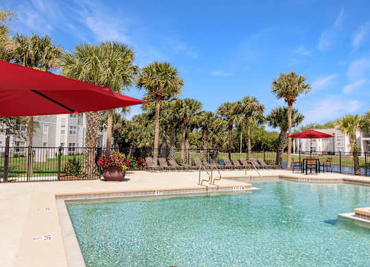 A pool surrounded by palm trees and a red umbrella.