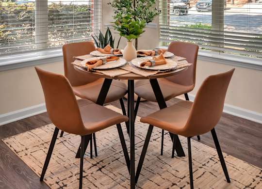 A dining table with chairs and a potted plant in front of a window.