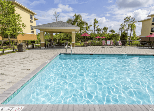 A pool with a gazebo and chairs around it. at Heron Pond 55+ Apartments, Florida