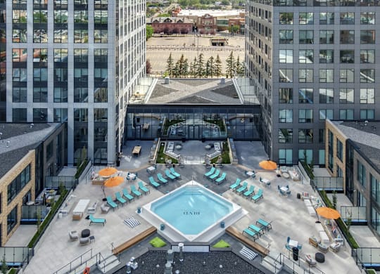A large swimming pool surrounded by sun loungers and umbrellas on a rooftop patio.