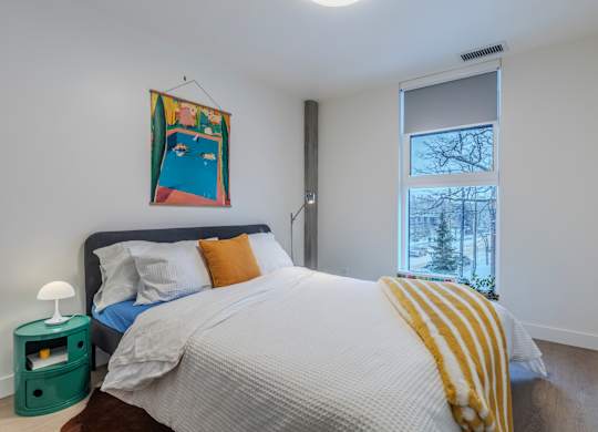 A bedroom with a bed, a nightstand, and a window.