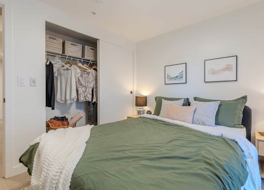 A bedroom with a bed, pillows, a nightstand, and a closet with clothes.
