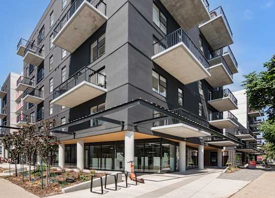 A modern multi-story building with balconies and a courtyard in front.