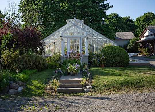 A white greenhouse is surrounded by a gravel driveway and a small garden.