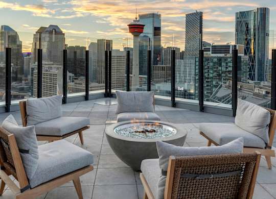 A rooftop patio with a fire pit and chairs overlooking a city skyline.